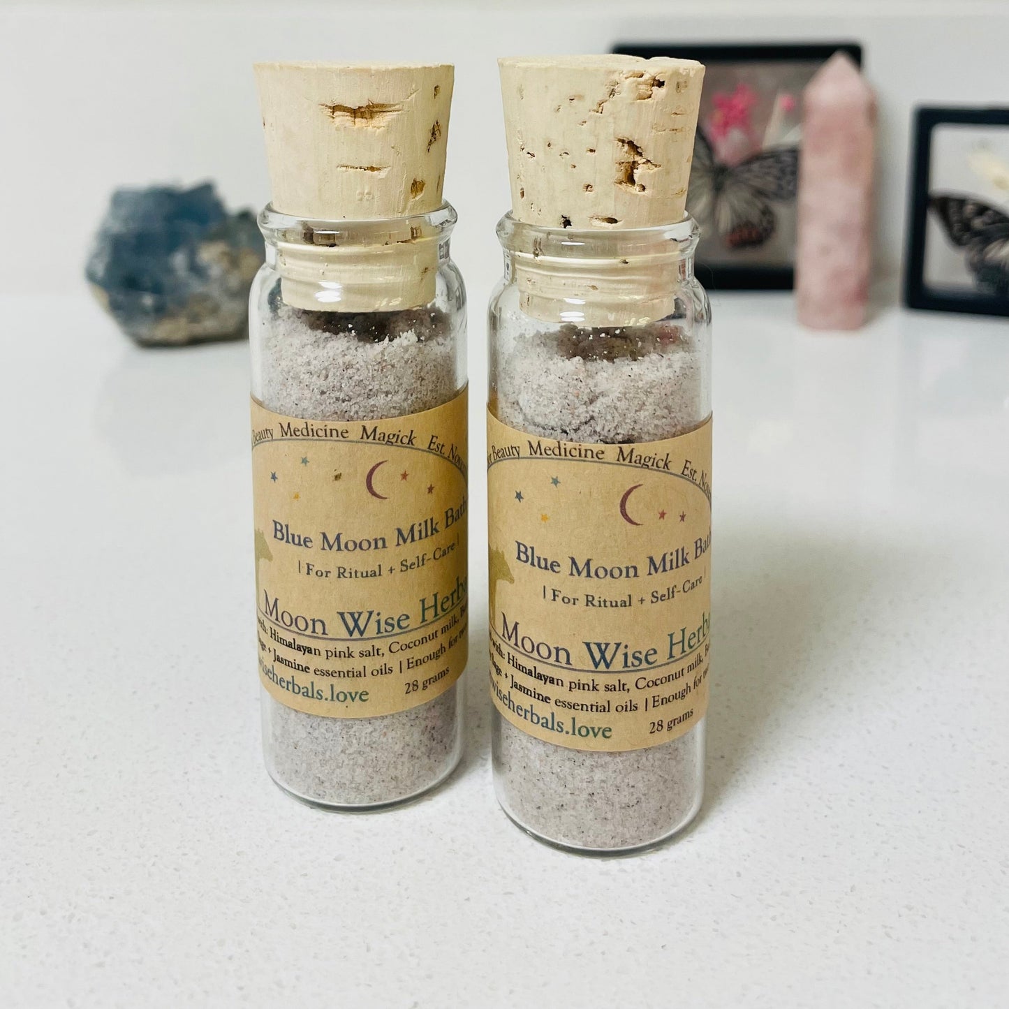 Two small glass bottles with cork lids containing 'Blue Moon Milk' on a light surface.