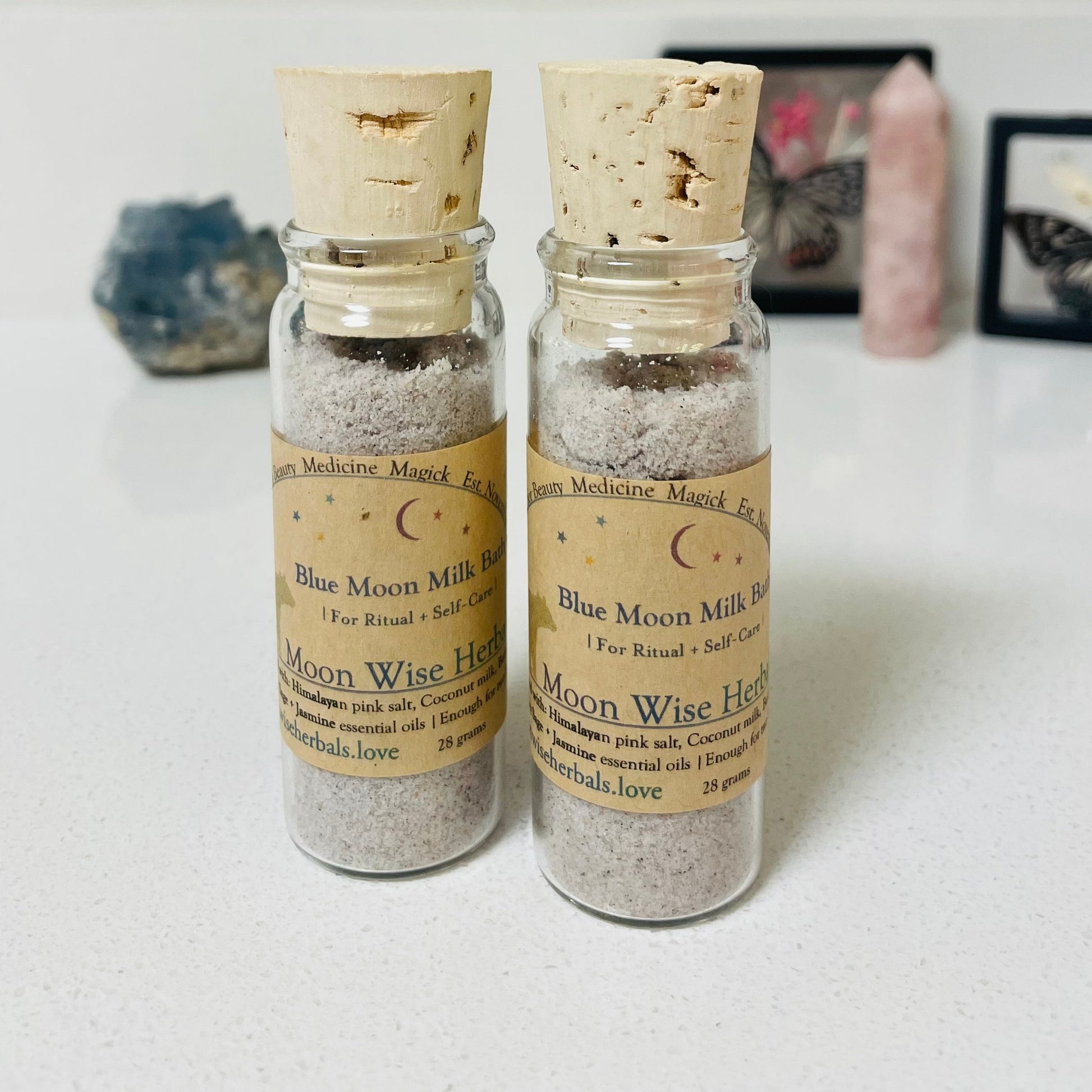 Two small glass bottles with cork lids containing 'Blue Moon Milk' on a light surface.