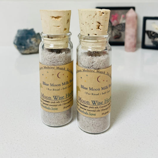 Two small glass bottles with cork lids containing 'Blue Moon Milk' on a light surface.