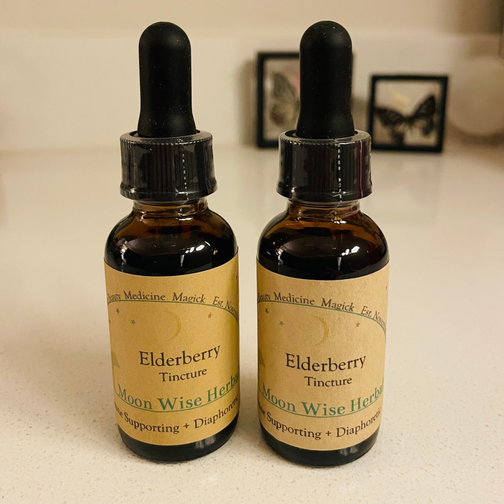 Two bottles of Elderberry Tincture from Moon Wise Herbs on a light surface.
